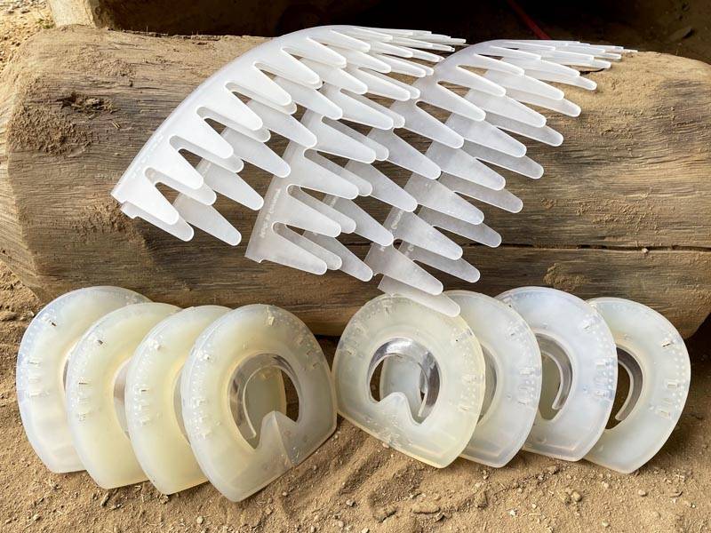 dummies of plastic horseshoes for practicing the correct welding technique are laid out in the sand in front of a tree trunk, accompanied by adhesive collars