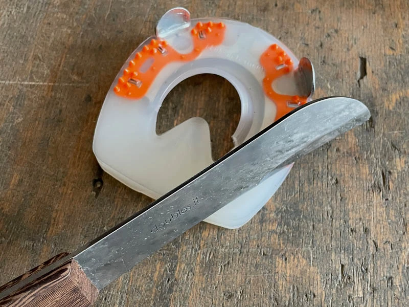 Dettaglio della lama del coltellaccio Kukri Double S. L'immagine mostra la lavorazione del rivestimento in plastica di un ferro composito per cavalli su un banco da lavoro.
