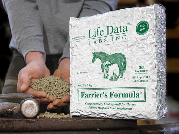 Packaging of the feed supplement Farrier's Formula from Life Data Labs for horses, with a farrier holding pellets. The product is placed on an anvil with hoof care tools in the background.