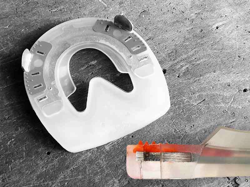 herradura alternativa con carcasa de plástico y soporte de ranilla apoyada sobre madera; también se puede ver una sección transversal de la estructura de agujeros para clavos en la herradura
