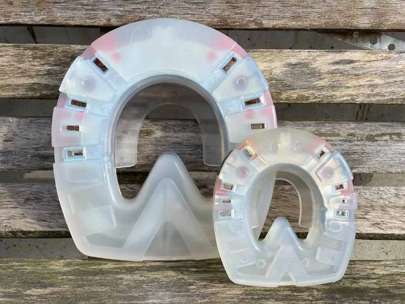 Un ferro di cavallo di plastica piccolo e uno grande, particolarmente stabile, si trovano uno accanto all'altro di fronte a una parete di legno.