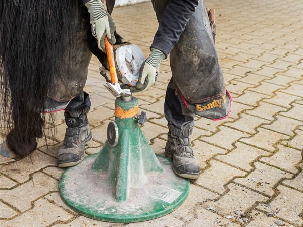 Maniscalco applica un ferro in plastica con anima in metallo sullo zoccolo di un cavallo. Lo zoccolo poggia sull'appoggio posteriore di un Hoofjack&reg; verde.