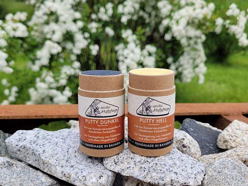 Putty chiaro e scuro di andis Hufpflege poggiano su pietre davanti a un arbusto fiorito