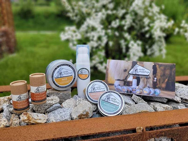 Putty, Shine, Polish, Mauke Balm e White Line Filler di andis Hufpflege stehen su pietre accanto al volantino del prodotto