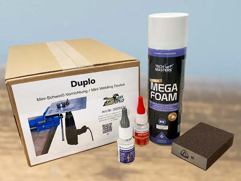 Hoof cleaner, abrasive block, super glue, and welding device from the medium starter set for glued horseshoes are placed on a wooden floor.