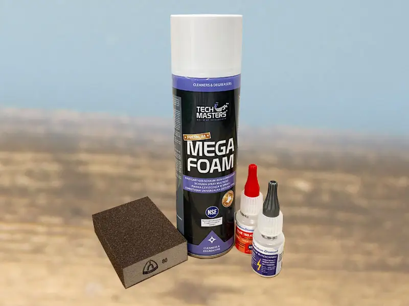 Hoof cleaner, sanding block, and super glue from the small starter set for gluing horseshoes are placed on a wooden floor.