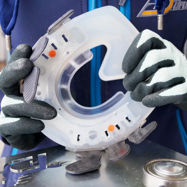 Close-up of a freshly plastic-welded glue-on horseshoe. The farrier is wearing protective gloves and guiding the composite horseshoe over the welding device in the area of the glued adhesive tabs.