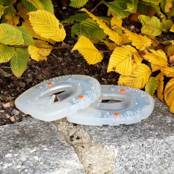 Two synthetic horseshoes with production-related soft knobs, orange dots, and a metal core are placed on a stone wall.