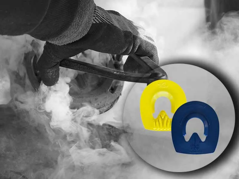 El herrador prueba la herradura en caliente, lo que genera una gran cantidad de humo. En la imagen también se muestra un detalle de la tapa azul y amarilla para herraduras.