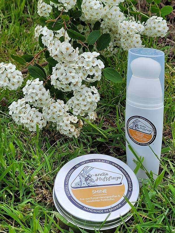 Polish et Shine de andis Hufpflege sont dans l'herbe devant un arbuste à fleurs