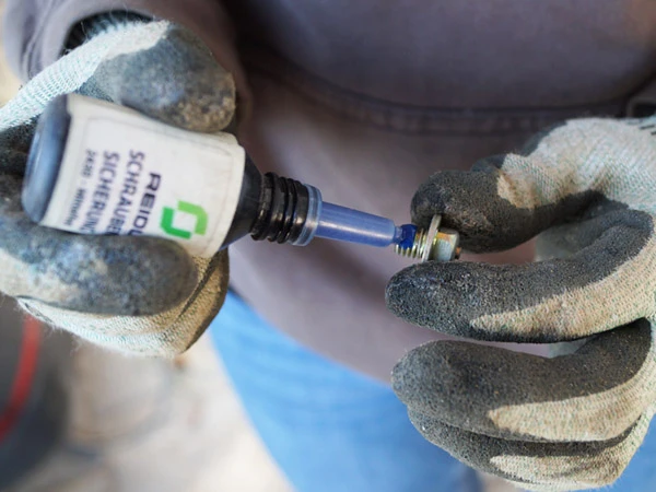 Gros plan lors de l’application d’une goutte de frein-filet EURO-LOCK sur un crampon antidérapant pour fer composite.