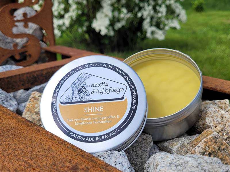 la boîte ouverte de Shine d'andis Hufpflege est posée sur des pierres