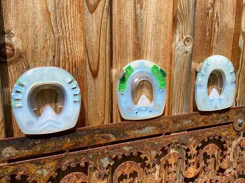 Trois fers sont posés sur une plaque métallique devant un mur en bois. On voit un fer ovale, un fer rond et un fer Straight Bar avec une pince légèrement droite.