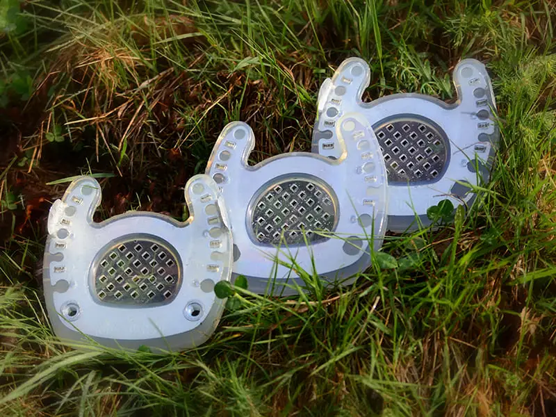 Trois fers ouverts à la pince sont posés côte à côte dans un pré. Ils présentent différentes versions avec ou sans pinçons et avec des trous pour crampons.