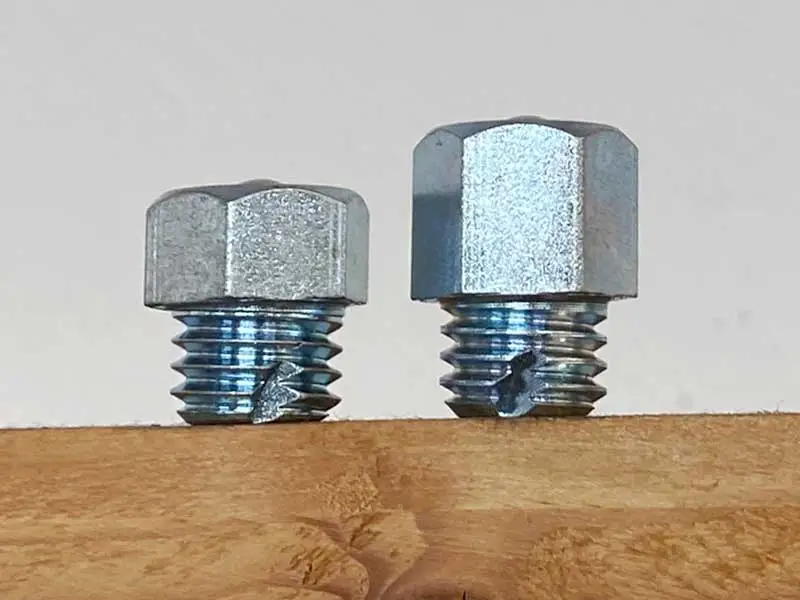 Due ramponi esagonali di altezze diverse con filettatura autofilettante sono posizionati su uno scaffale in legno.