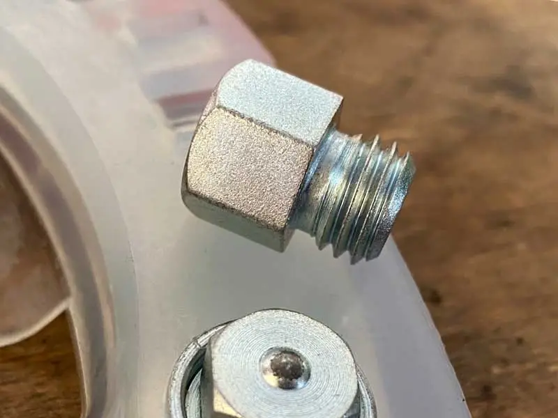 Un rampone senza filettatura autofilettante è posato su una ferratura composita per cavalli; un altro rampone è già avvitato nel foro per ramponi della ferratura.