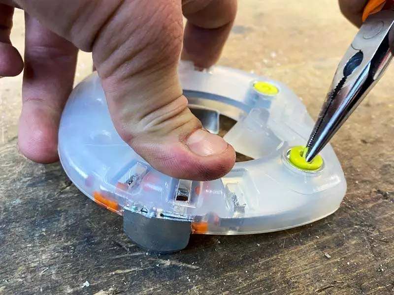 Con un oggetto appuntito viene rimosso un tappo giallo in plastica, un cosiddetto tappo di chiusura, dal foro per ramponi del ferro.