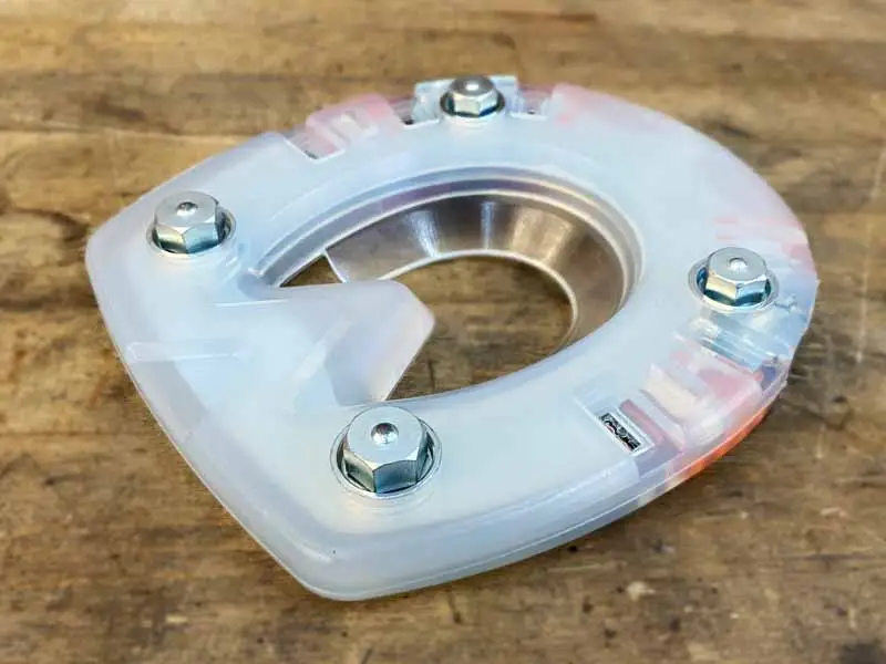 Una speciale ferratura composita ammortizzante per il salto ostacoli con quattro fori per ramponi è posata su un pavimento in legno; sono avvitati quattro ramponi esagonali.