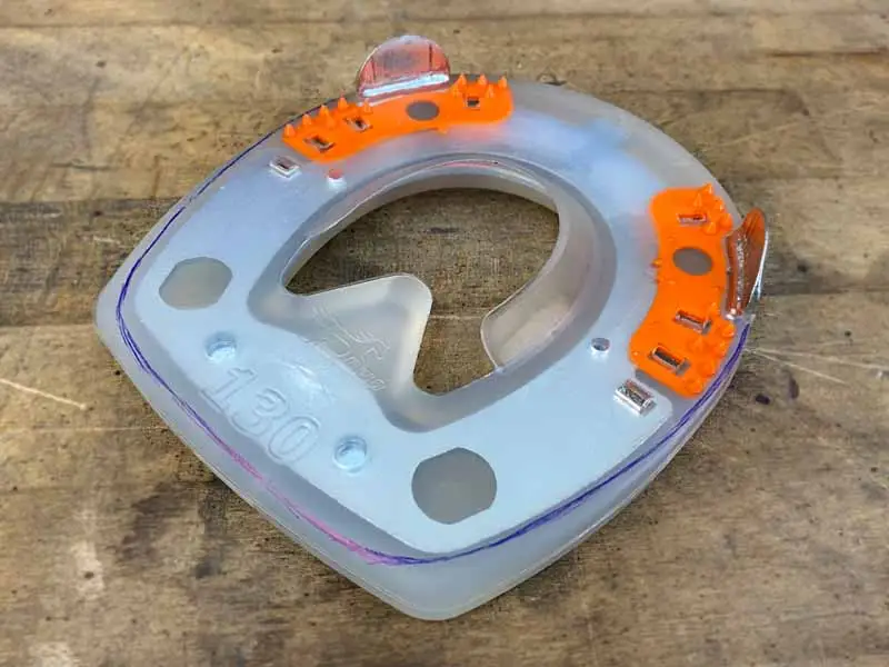 Un Straight Bar Shoe avec gaine en plastique est posé sur une planche en bois. La forme du sabot est marquée au stylo bleu pour permettre l'adaptation du fer.
