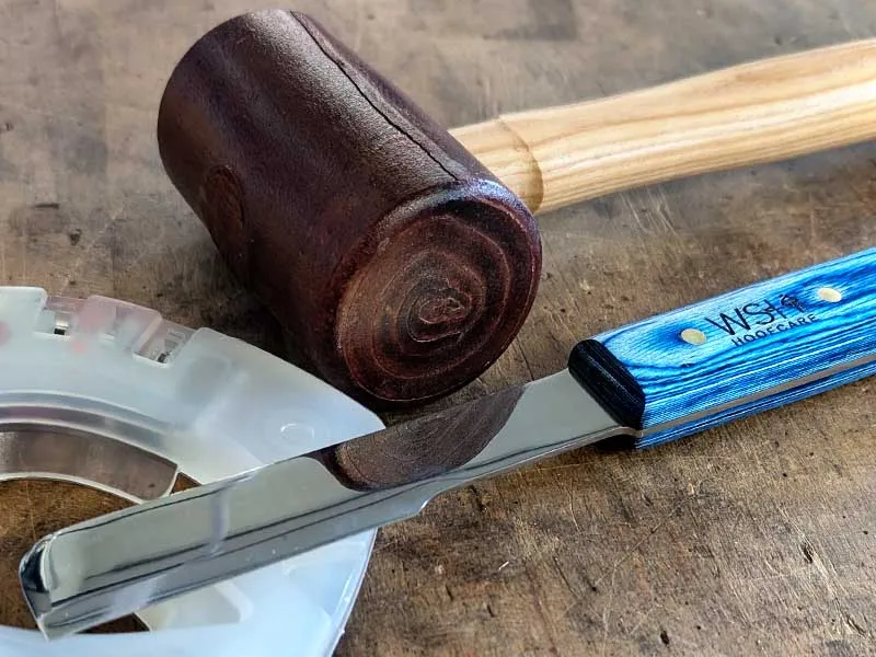 Sul banco da lavoro sono presenti un ferro di cavallo alternativo, una mazzuola con la testa in pelle di bufalo e un coltellaccio a forma di ascia della WSH Hoofcare.
