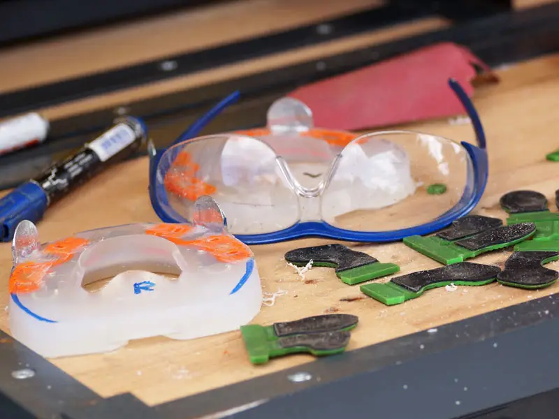 Schutzbrille, Edding, Schleifpapier, Grundplatten und Klebelaschen liegen auf einer Werkbank